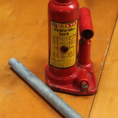 Vintage Norco KYB 1.5-ton hydraulic bottle jack in red paint, complete with its metal handle bar.