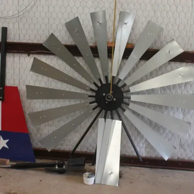 Decorative metal windmill head with galvanized blades, accompanied by a painted Texas flag tail vane.
