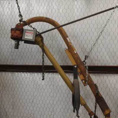 Vintage yellow 3-point post hole digger attachment for a tractor, showing some surface rust and wear from use.