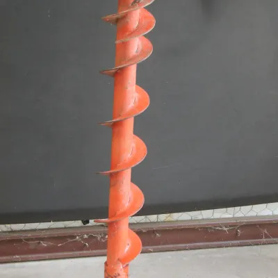 Vintage orange metal earth auger drill bit, showing some wear and dirt from use.