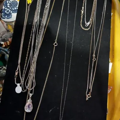 Assortment of fine silver and gold-tone chain necklaces, including two with teardrop-shaped gemstone pendants, displayed on a black...