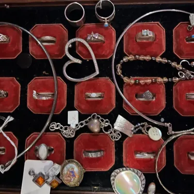 Assorted sterling silver and costume jewelry collection, including rings, bracelets, necklaces, and pendants, displayed in a red...