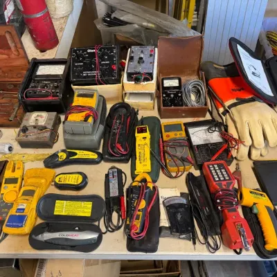 Assortment of vintage and modern electrical testing equipment, including multimeters, clamp meters, and various hand tools.