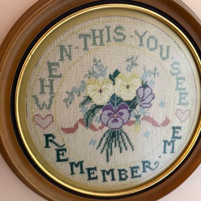 Vintage framed cross-stitch sampler featuring a floral bouquet and the phrase 'When This You See Remember Me' in a round wooden...