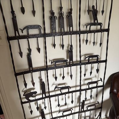 Large wrought iron decorative screen featuring stylized figures, animals, and arrow motifs in a rustic, folk art style.