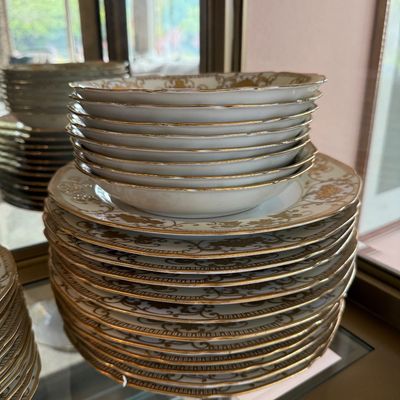 Vintage porcelain dinnerware set featuring intricate gold filigree borders and scalloped rims, including stacks of dinner plates and...
