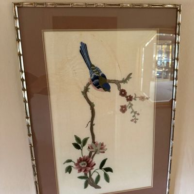 Framed Asian silk embroidery depicting a blue bird perched on a flowering branch, housed in a silver-toned faux bamboo frame with a mauve...