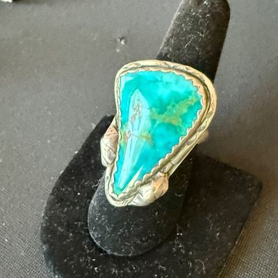 Vintage Southwestern sterling silver ring featuring a large, triangular turquoise stone with a serrated bezel and leaf accents, displayed...