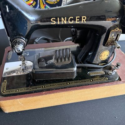 Vintage Singer 99K sewing machine with black finish, gold decals, and foot pedal, mounted in its original wooden carrying case base.