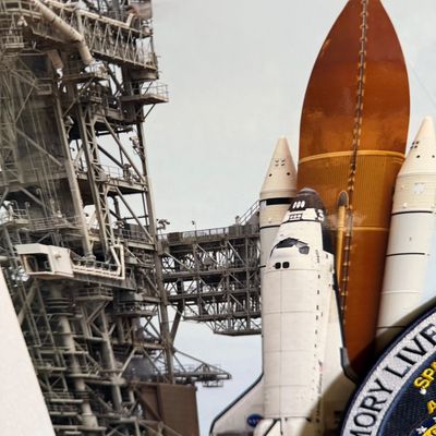 Framed photograph of a Space Shuttle launch on the pad, featuring an embroidered commemorative patch in the corner.