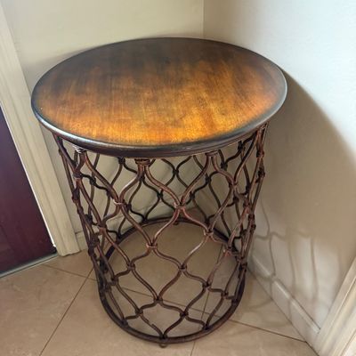 Round accent table featuring a warm wood-toned top with a dark-stained edge, supported by an openwork metal base in a woven lattice design.