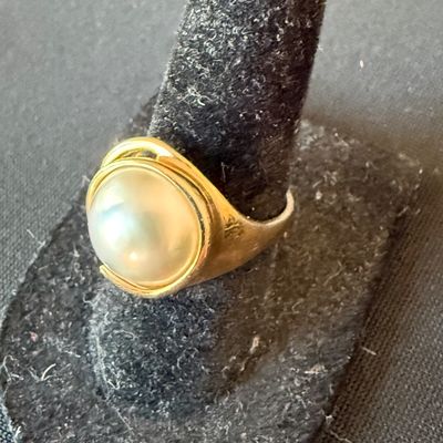 Vintage gold ring featuring a large, bezel-set faux pearl, displayed on a black velvet ring stand.