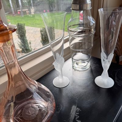 Vintage glassware collection featuring a pink depression glass decanter, a pair of champagne flutes with frosted hummingbird stems, and a...