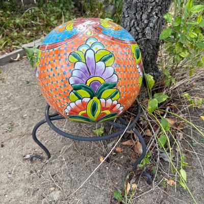 Talavera ceramic garden sphere featuring vibrant hand-painted floral motifs in orange, blue, and green, displayed on a black wrought iron...