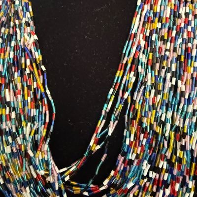 Multi-strand seed bead necklace featuring a vibrant mix of colorful glass bugle beads, gathered at a brass-tone bar clasp.