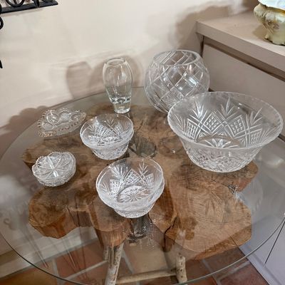 Collection of cut glass and crystal tableware, including bowls, a vase, and small dishes, displayed on a rustic wood slice and glass-top...