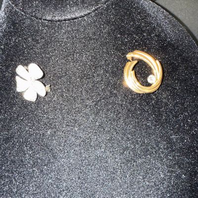 Two vintage brooches displayed on a black velvet stand, featuring a silver-tone four-leaf clover pin and a gold-tone circular swirl pin...