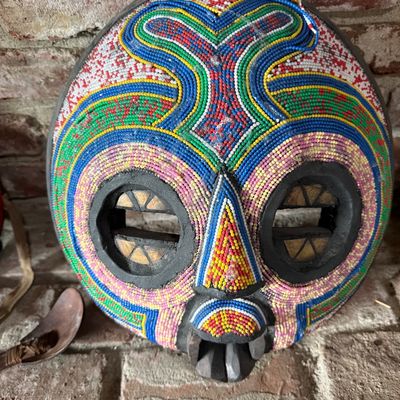 Handcrafted African-style beaded mask featuring vibrant, multi-colored beadwork in geometric patterns over a dark wooden base.