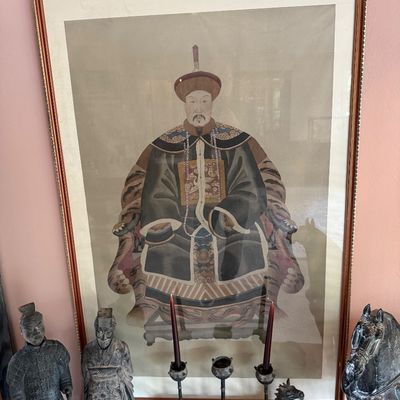 Large framed Chinese ancestor portrait depicting a seated official in traditional Qing dynasty robes, displayed behind a collection of...