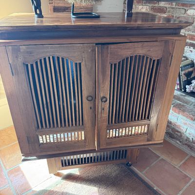 Rustic wooden cabinet featuring slatted double doors, a lower slatted shelf, and a warm, distressed finish.