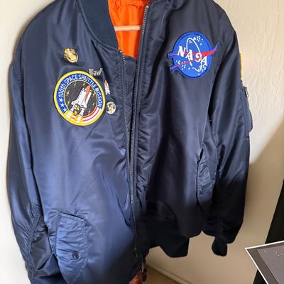 Navy blue MA-1 style bomber jacket with a bright orange lining, featuring a NASA logo patch, a 100th Space Shuttle Mission patch, and...
