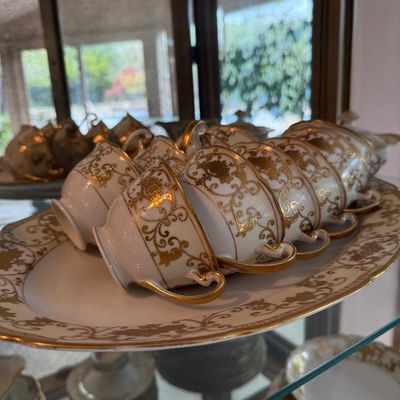 Vintage white porcelain teacups and matching serving platter featuring intricate gold filigree scrollwork and gilded handles.