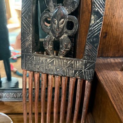 Hand-carved African wooden comb featuring a stylized mask motif on the handle with geometric etched details.