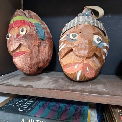 Pair of vintage hand-carved coconut heads with painted details and shell eyes, displayed on a wooden shelf.