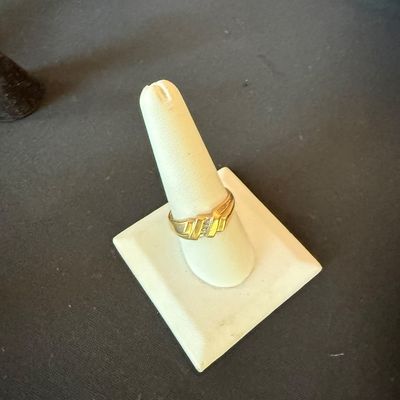 Gold band ring featuring a textured, geometric design with a small central accent stone, displayed on a white ring cone.