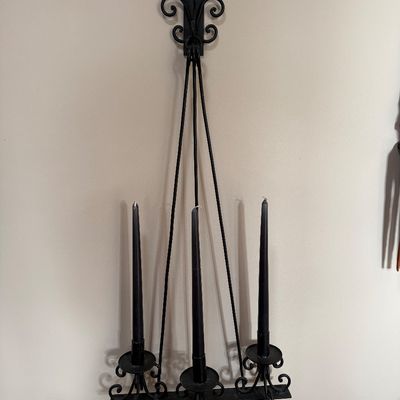 Vintage black wrought iron three-light wall sconce featuring scrollwork details and holding three black taper candles.