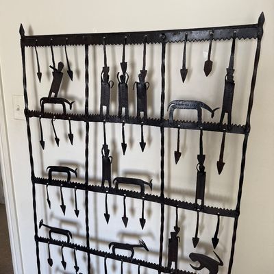 Wrought iron wall hanging featuring stylized figures, animals, and arrow motifs in a rustic, folk art style.