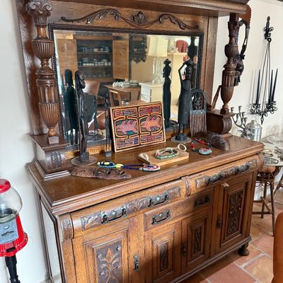 Antique carved oak sideboard with a mirrored hutch top, featuring ornate columns, decorative paneling, and a collection of African-style...