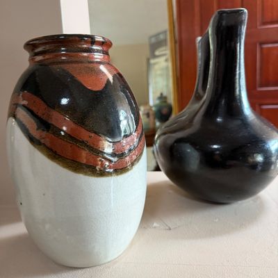 Two ceramic art pottery vessels, including a white, brown, and black glazed vase alongside a black-glazed double-spout wedding jug.