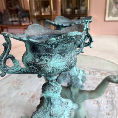 Ornate cast metal urns with a heavy green verdigris patina, featuring decorative handles and intricate relief details.