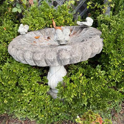 Vintage concrete birdbath featuring a scalloped basin adorned with three small concrete bird figures, set on a decorative pedestal base.