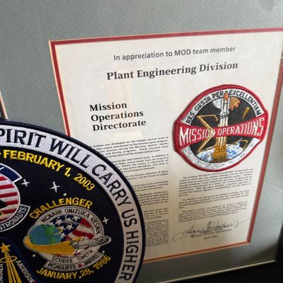 Framed NASA Mission Operations Directorate appreciation certificate with patch, displayed alongside a large commemorative space shuttle...