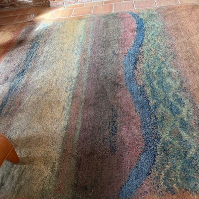Large area rug featuring an abstract, multi-colored landscape design with earthy tones, blue, and green accents.