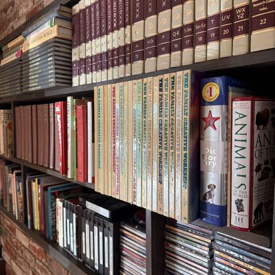Dark wood bookshelves filled with vintage book sets, including a 22-volume World Book Encyclopedia set, "The Family Creative...