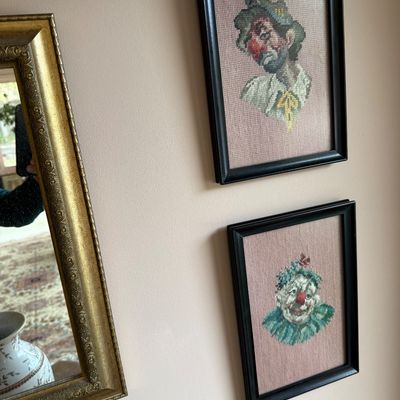 Pair of vintage framed needlepoint portraits depicting sad and happy clowns, housed in simple black frames.