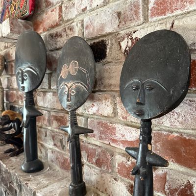 Three vintage Ashanti Akua'ba wooden fertility dolls with dark finishes, displayed on a brick mantel.