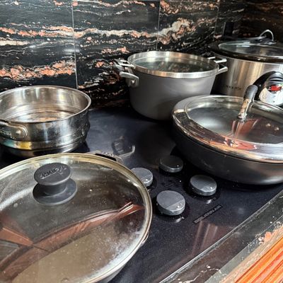 Assorted cookware on a Jenn-Air cooktop, including an All-Clad saucepan, a Lodge skillet with glass lid, a Calphalon stockpot, and a...