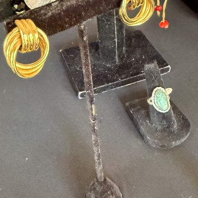 Vintage gold door knocker style earrings displayed on a black velvet stand, shown alongside a silver-tone ring with a green...