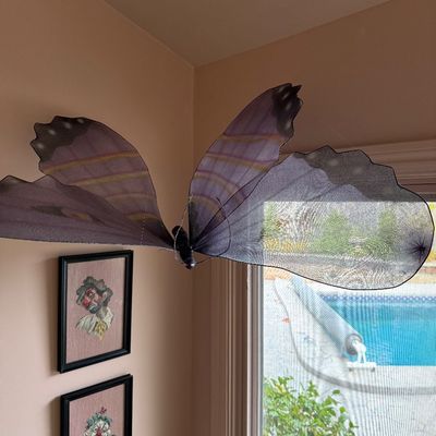 Large decorative hanging butterfly with purple mesh wings, shown suspended near a window.