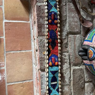 African Yoruba beaded sash featuring intricate geometric patterns, stylized figures, and a border of cowrie shells.