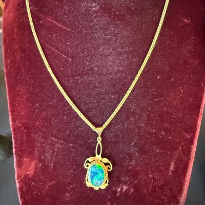 Vintage gold necklace featuring an ornate pendant set with a vibrant, oval-cut blue-green opal cabochon, displayed on a red velvet bust.