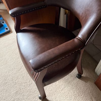 Vintage captain's style office chair upholstered in dark brown faux leather with brass nailhead trim and caster wheels.