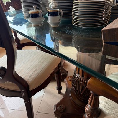 Traditional dining set featuring a glass-top table with a carved wooden pedestal base, accompanied by upholstered chairs and a large set...
