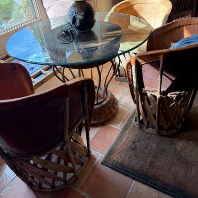 Rustic Mexican equipal dining set featuring a round glass-top table with a carved pedestal base and three matching leather and wood...