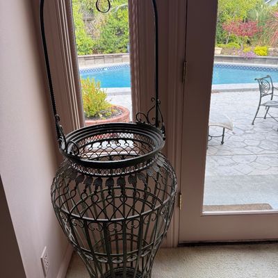 Ornate wrought iron floor planter stand featuring a tall decorative arch with scrollwork details.