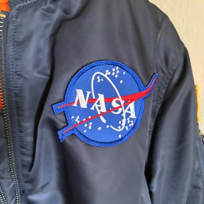 Vintage MA-1 style navy blue flight jacket featuring an embroidered NASA "meatball" logo patch on the chest.